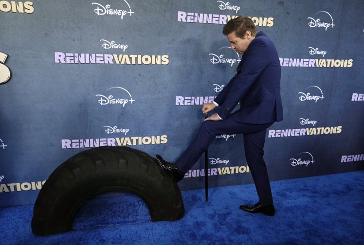 傑瑞米雷納拄著拐杖出席主演實境秀「舊車大改造」洛杉磯首映會，一腳踩上輪胎重現劇中經典場面。(美聯社)