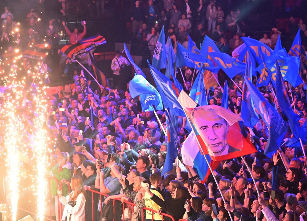 在俄羅斯鄂木斯克舉行的國際勞動節音樂會上，人們揮舞著旗幟，其中一面有普丁肖像。 ...