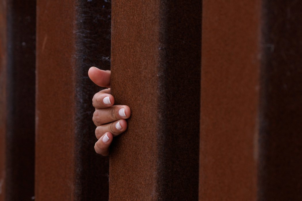 美國加州聖地牙哥附近的邊境圍籬，一名移民女孩朝美國方向伸手。 圖／路透社