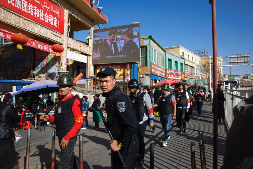 新疆和闐街頭，警察正在巡邏，背後螢幕上放映中國國家主席習近平的影片。 圖／美聯社...
