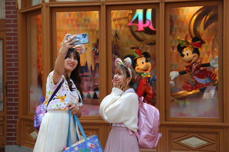 圖為兩名女遊客在東京迪士尼樂園，戴上造型髮圈開心自拍。新華社