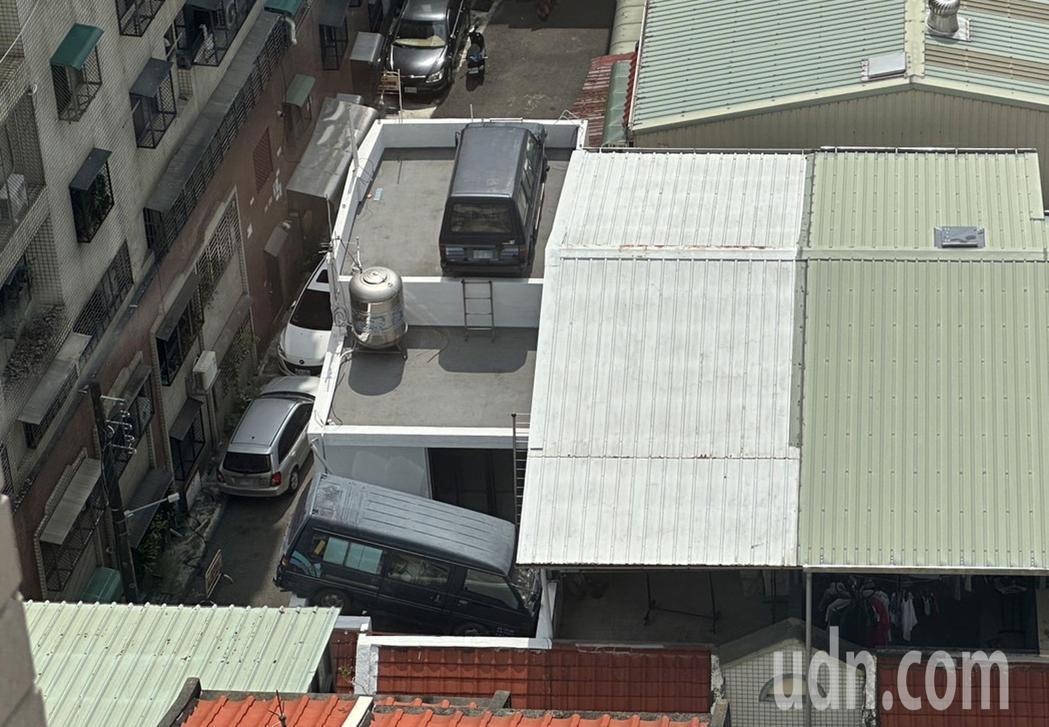 台中市北區一棟透天厝頂樓放置二輛廂型車，其中一輛車尾卡在女兒牆上，嚇壞鄰居。記者...