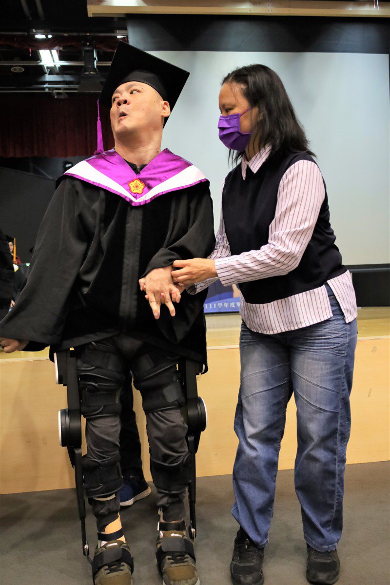 亞洲大學博士生陳銘哲（左）穿著「外骨骼機器人」領獎，右為始終陪伴他的大姊陳秀玉。圖／亞洲大學提供