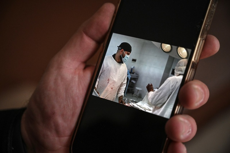謝赫醫師盯著手機螢幕上自己過去在烏克蘭動手術救治患者的照片。圖／取自紐時
