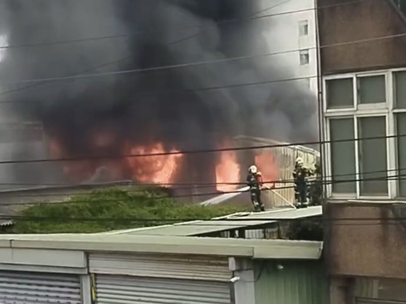 竹東鎮沿河街一處平房冒出大火，消防人員冒險站在鄰房屋頂灑水灌救。記者巫鴻瑋／翻攝