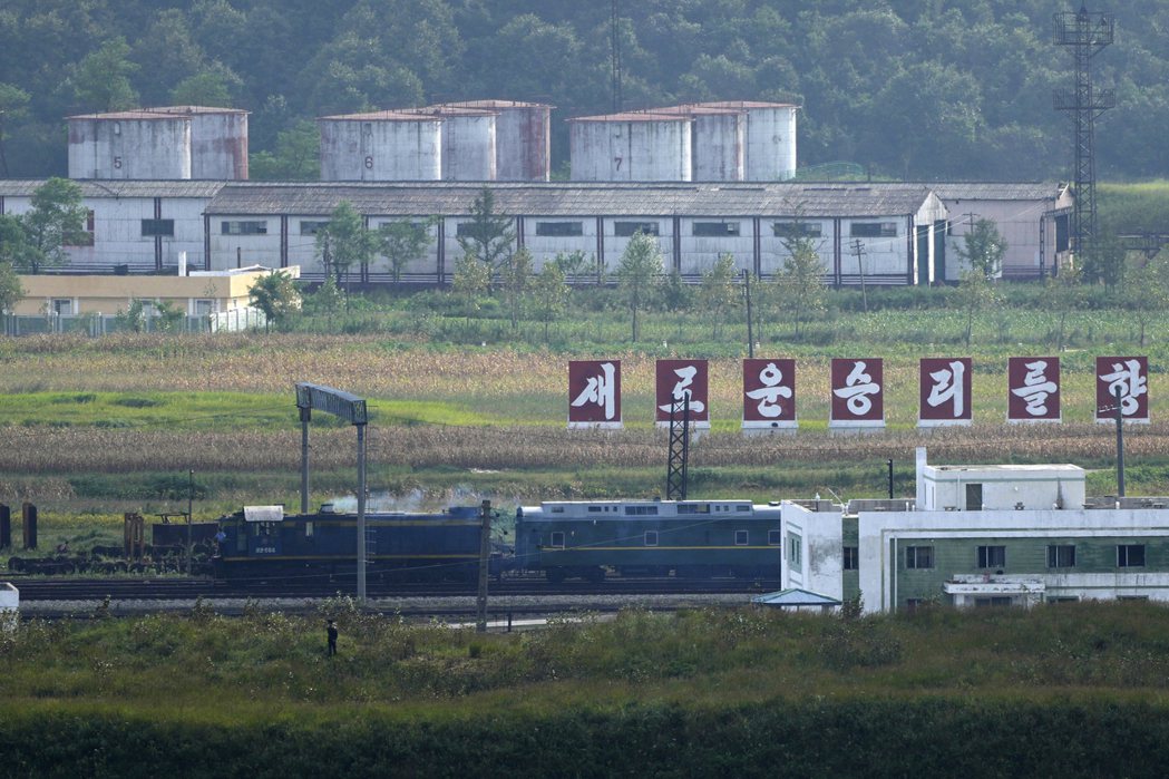 一列帶有黃色裝飾的綠色火車在北韓與俄羅斯邊境上行駛，經過寫著「邁向新勝利」的標語...