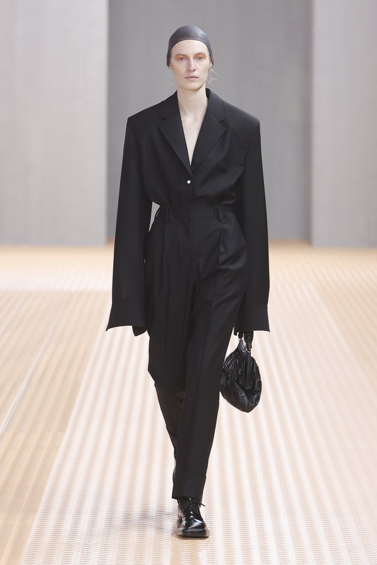 第47套壓軸的服裝，女模全身黑色，但具有寬大超長袖的西裝上衣搭配褲裝、手提包，展現出某種中性、自信的雋永印象。圖／Prada提供
