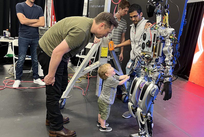 人形機器人Optimus學會站立走路是一大創舉，與馬斯克剛剛學會走路的兒子X相見歡。 （天下雜誌出版提供）