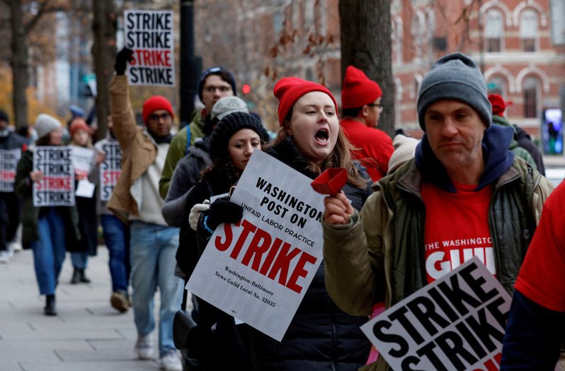 華盛頓郵報員工7日在辦公室外揮舞標語，抗議「工資太低」罷工一天。（路透）