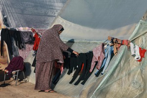 一名巴勒斯坦婦女12月16日在加薩南部拉法的帳篷外曬衣服，以哈戰爭爆發後，現在有錢也租不到房屋。法新社