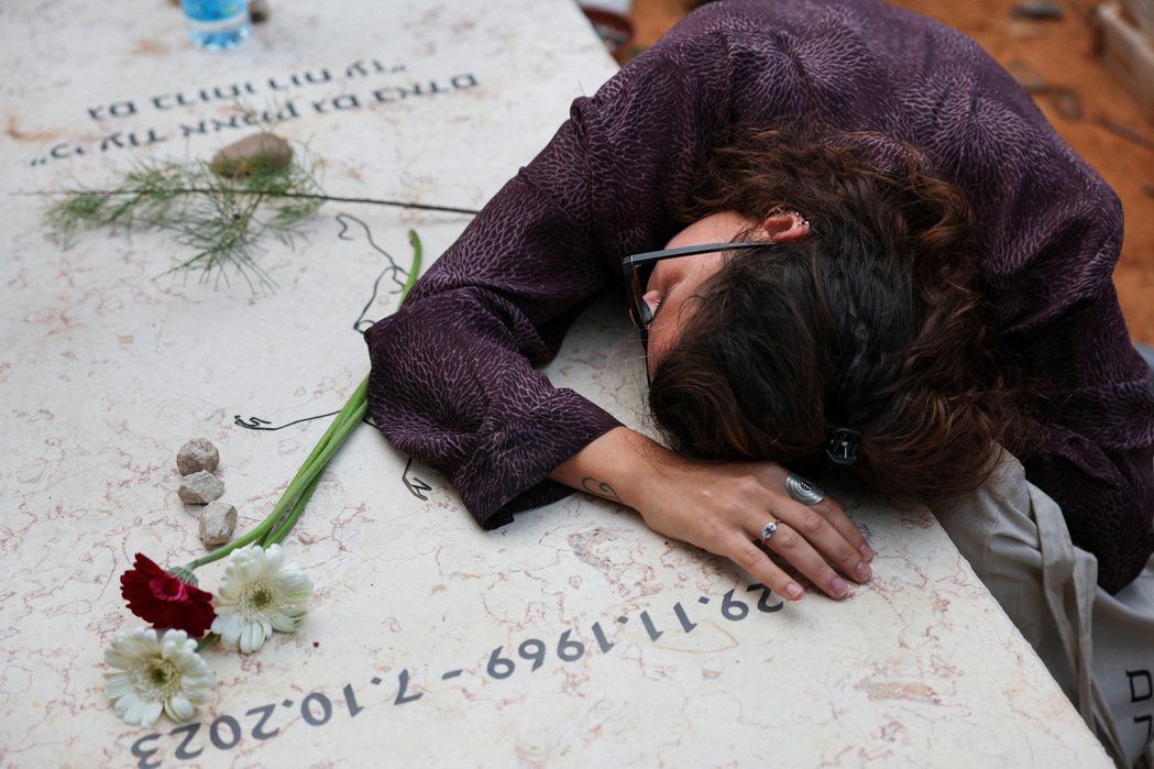 參加沙姆里茲葬禮的哀悼者，伏在墓園中另一座10月7日突襲中死去的罹難者墳墓上悼念...