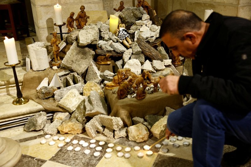 以色列今天轟炸遭圍困的加薩地區，身處加薩的巴勒斯坦人直言，今年耶誕節「沒有絲毫喜悅」。圖為以色列伯利恆的福音路德教會，男子在一個裝置上點燃蠟燭，該裝置上有一個象徵嬰兒耶穌的雕像躺在石窟的廢墟中。路透