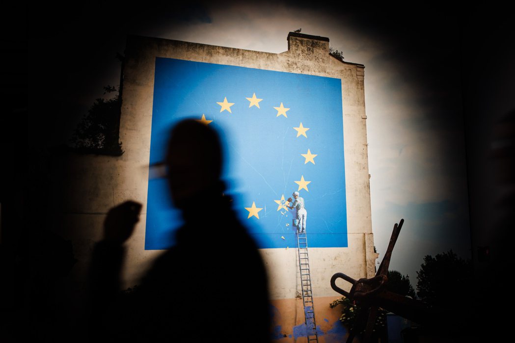 英國塗鴉藝術家Banksy在英國脫歐後創作壁畫，從歐盟旗的12顆星中敲下1顆，比...