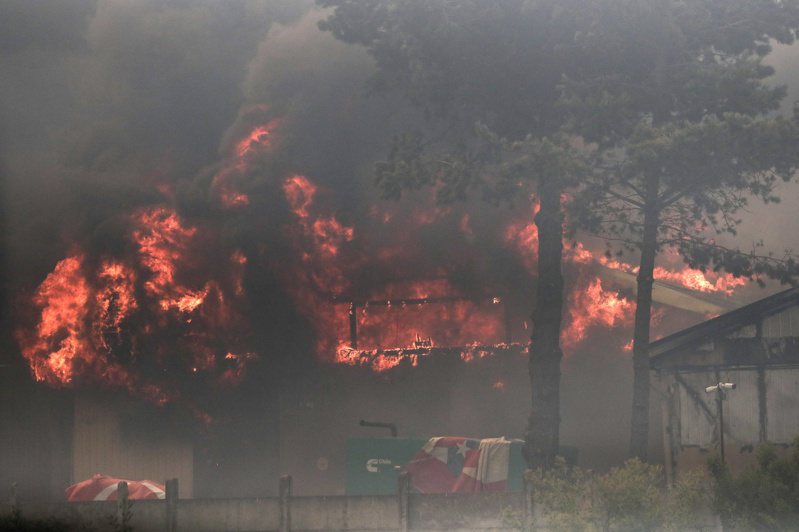 智利有關當局今天表示，中部地區的森林大火已奪走至少51條人命，且死傷數據可能會進一步攀升。圖為智利瓦爾帕萊索地區比納薩瑪的森林火災，工業區的一棟建築被大火燒毀。法新社
