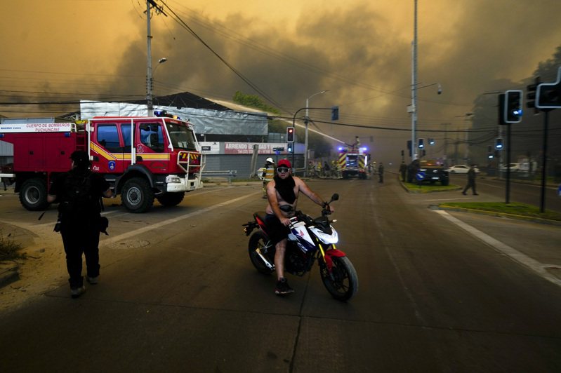 智利中部野火造成的罹難人數已增至64人，比納薩瑪巿一居民騎著摩托車疏散，消防隊員噴水保護建築物。 美聯社
