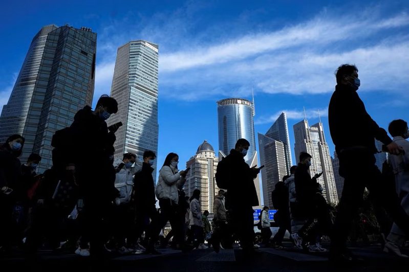 IMF 將大陸2024年經濟成長預測上調至4.6%，圖為上海陸家嘴金融區，人們穿過辦公大樓附近的街道。路透