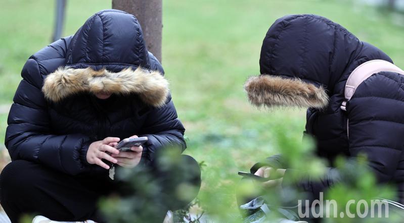 強烈冷氣團南下，各地氣溫明顯下降，尤其北台灣感受明顯，到公園踏青民眾在寒風中，穿戴保暖外套及連身帽，低頭滑手機打發時間。記者侯永全／攝影