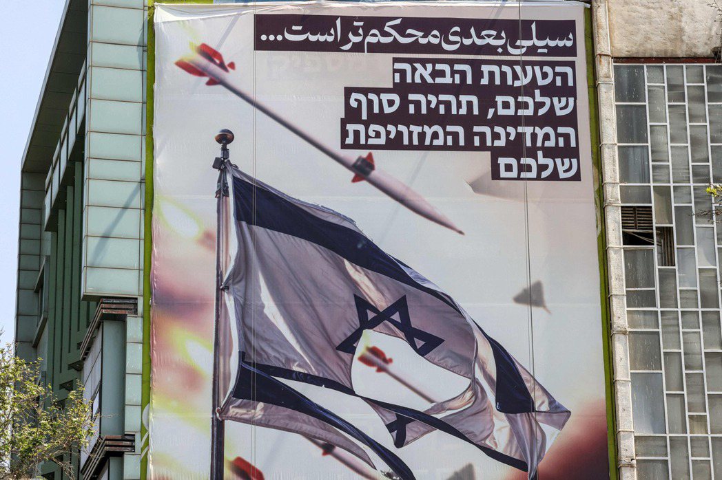伊朗首都德黑蘭街頭的一幅橫幅，上面畫著導彈和無人機飛過撕破的以色列國旗，上面用波...