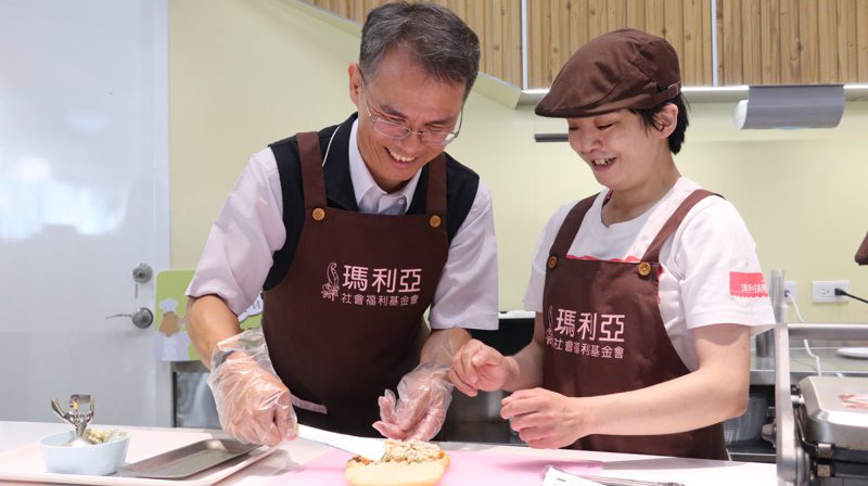 台中市劳工局副局长罗群穆（左）担任一日店长，和玛利亚青年小倩手作轻食三明治。图／玛利亚基金会提供