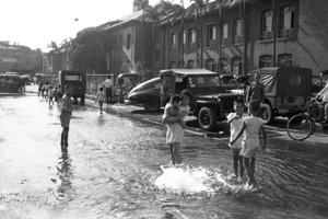 1959年5月8日，台北市長安西路市府大廈門口的自來水管破裂，導致街道積水，附近孩童利用這個機會嬉水避暑。圖／聯合報系資料照片