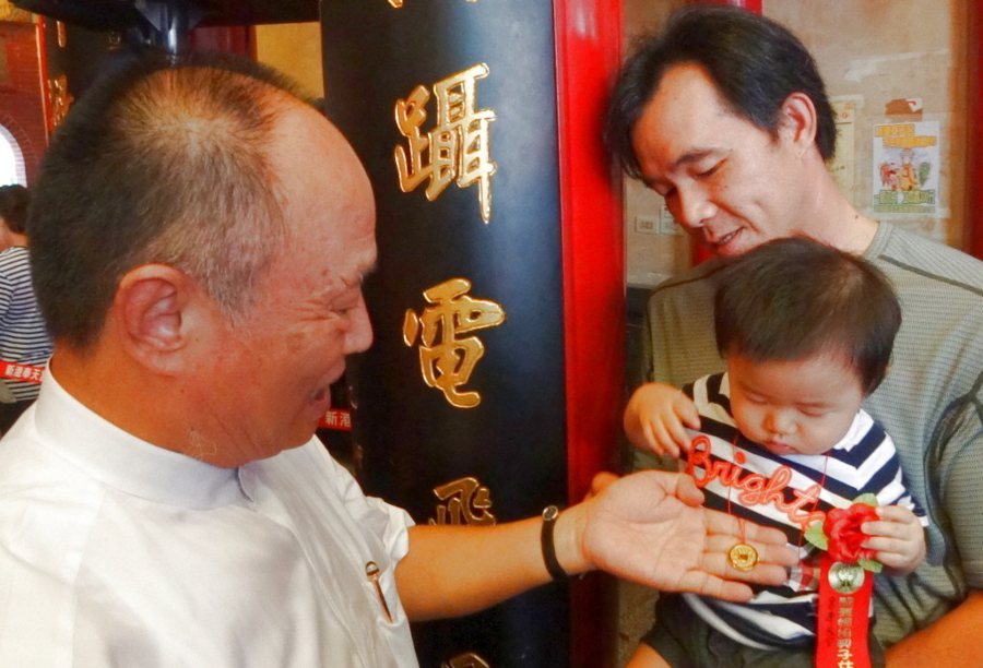董事長何達煌（左）把穿有紅絲線的貫錢掛在幼童身上。聯合報系資料照／記者陳永順攝影