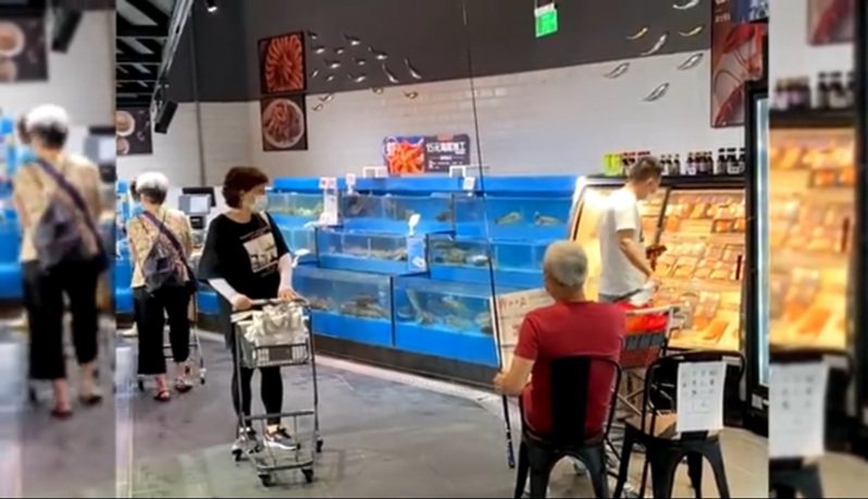 上海一間超市，一個老先生坐在販賣鮮魚的魚缸前釣魚，獨特畫面引發熱議。（視頻截圖）