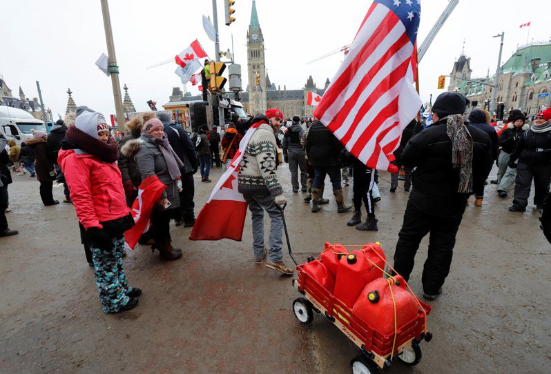 加拿大反強制接種疫苗示威中，6日在渥太華國會前，有披著加拿大國旗的男子拖著燃料罐，旁邊另有示威者舉著美國國旗。圖／路透