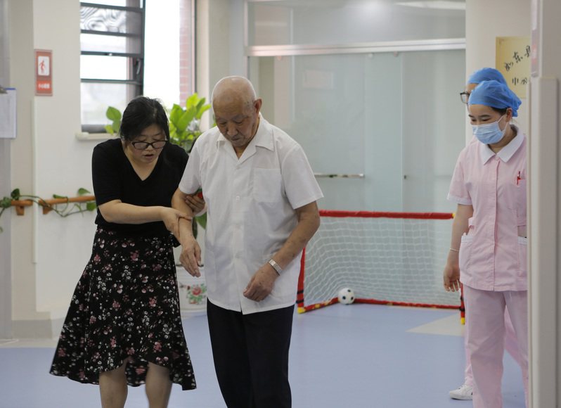 中國退休養老金政策改變，老人須自證「活著」，才能繼續領取退休金。圖為
江蘇一家護理院，工作人員攙扶老人行走。(新華社)