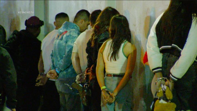 一排男女戴著手銬、面對牆壁站著，正在接受警方調查。（Keynews.tv）
