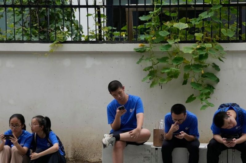 中國日前公布擬加強整頓網路遊戲後，衝擊整個行業。圖為北京街頭年輕人在玩手機。美聯社