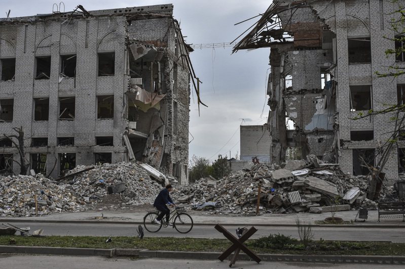 一名婦女18日在烏克蘭前線城鎮奧里希夫，騎自行車經過一棟被俄羅斯空襲摧毀的建築物前。(美聯社)