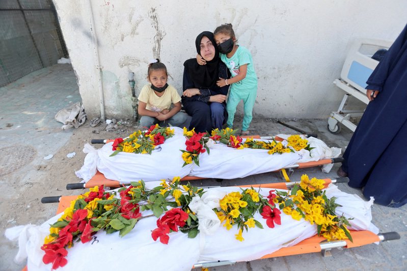在加萨走廊南部汗尤尼斯，加萨人正努力将埋葬在纳瑟医院的巴人尸体搬入墓地，并在尸体旁哀悼。（路透）